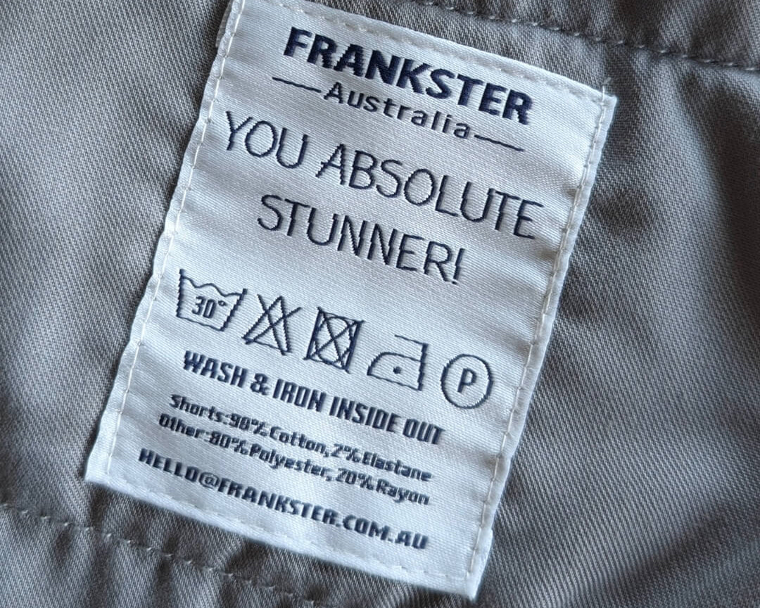 Close-up of a Frankster Men's Shorts care label on grey cotton and elastane fabric with washing instructions