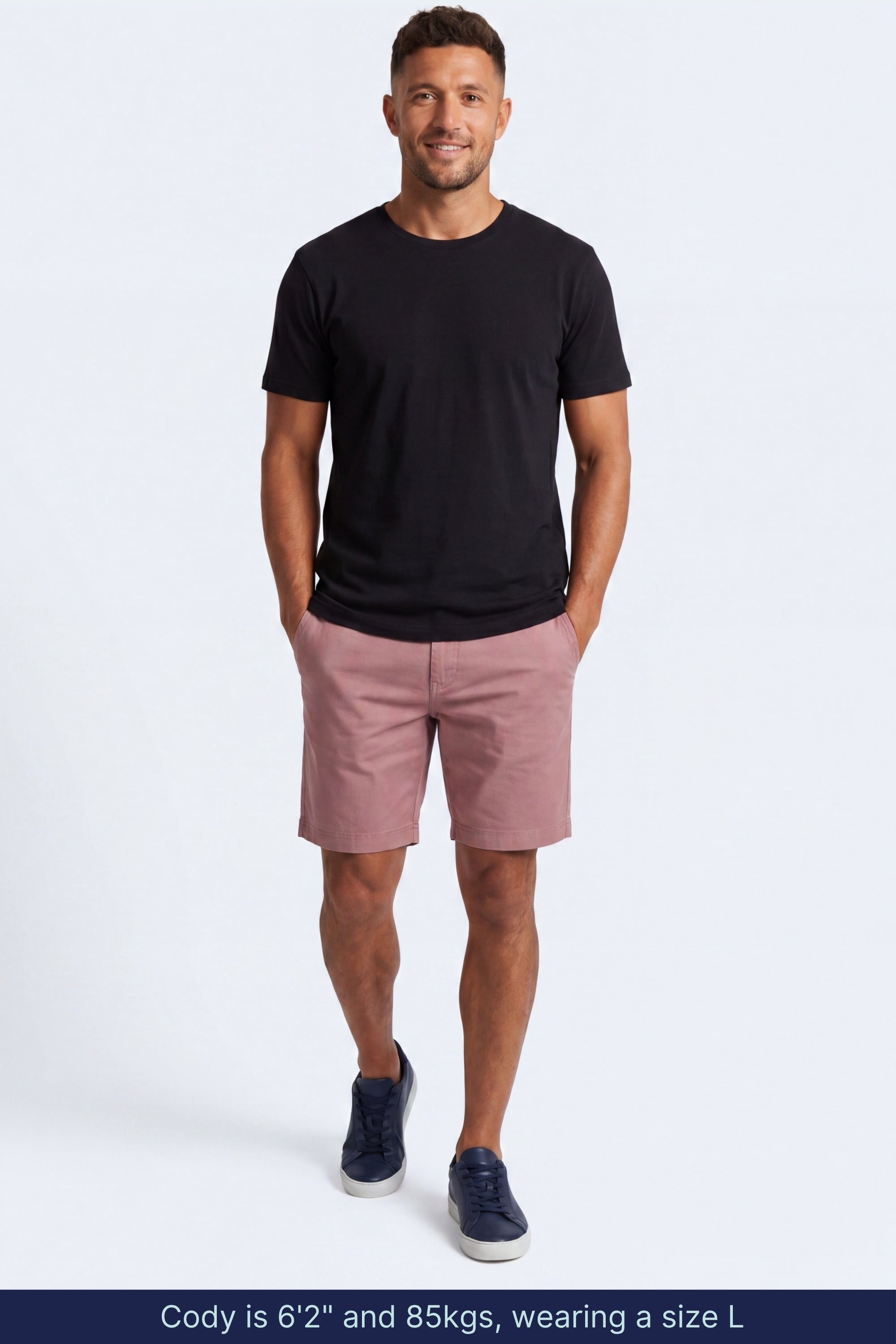 Man wearing muted pink cotton blend Sundowners * The Everydays men's shorts by Frankster, paired with a black t-shirt and navy sneakers.