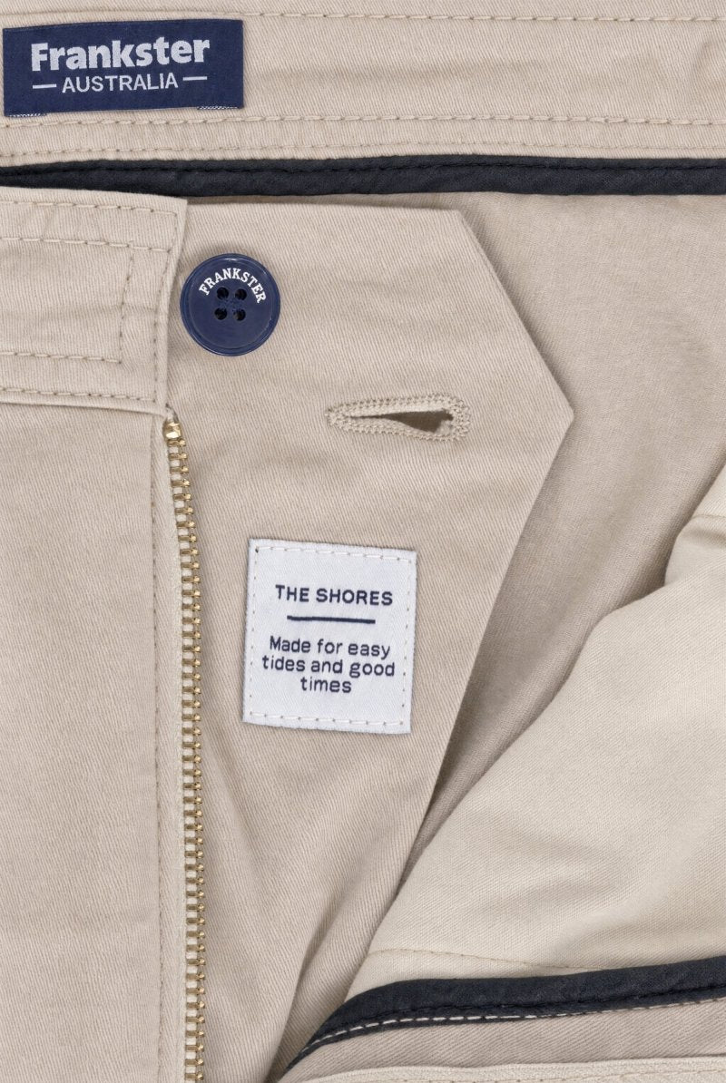 Close-up of beige men's shorts "Shores * The Everydays" by Frankster showing button, zipper, and label sewn inside made from soft, durable cotton material.