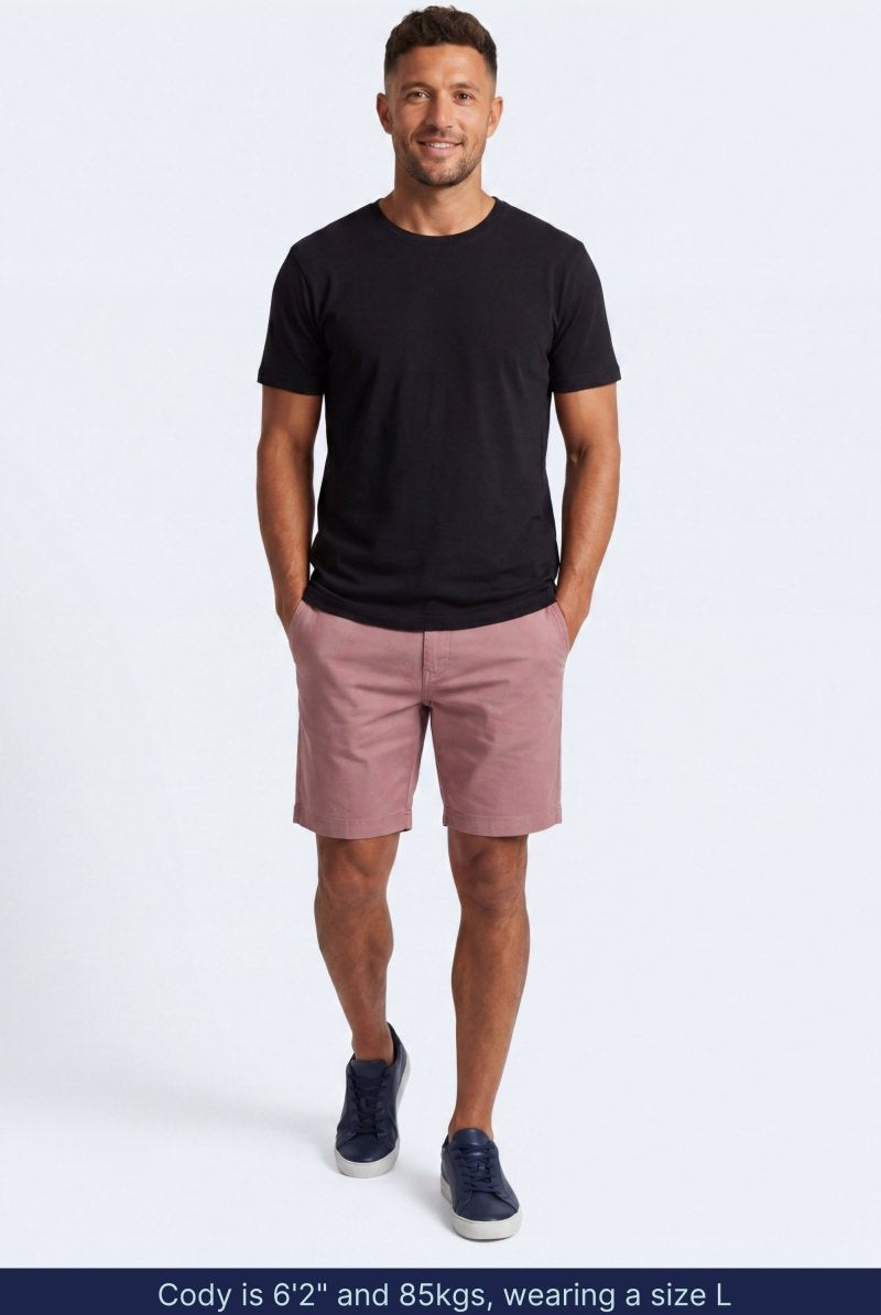 Man wearing muted pink cotton blend Sundowners * The Everydays men's shorts by Frankster, paired with a black t-shirt and navy sneakers.