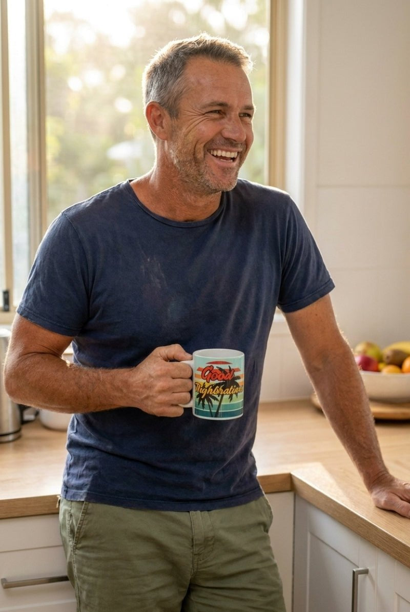 Man wearing casual olive-green men's shorts and a worn navy-blue t-shirt, holding The Good Thighbrations Mug in a bright kitchen setting, showcasing relaxed comfort linked to Frankster men's shorts.
