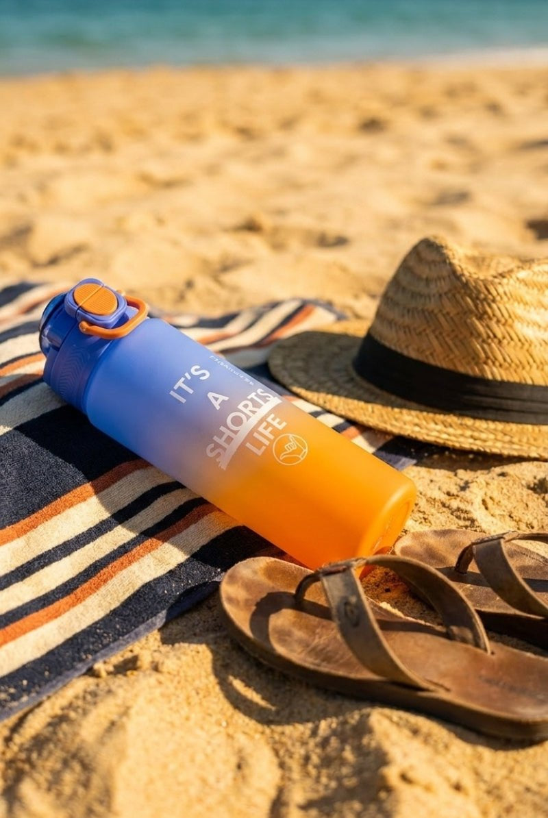 Water Bottle Orange Blue resting on a striped towel beside a straw hat and worn sandals on sandy beach, evoking casual men's shorts day.