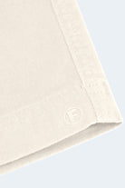 Close-up of the edge of a beige fabric, showcasing stitching details and a small, embossed letter "F" near the corner. The background is a light, solid color, highlighting the texture and craftsmanship of the fabric.