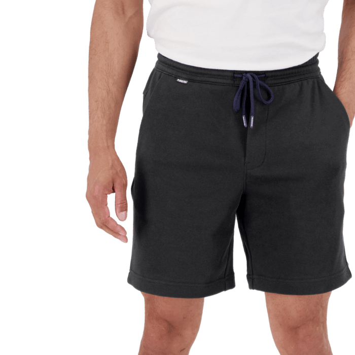 Man wearing black drawstring shorts and a white t-shirt with hands relaxed by sides against plain background