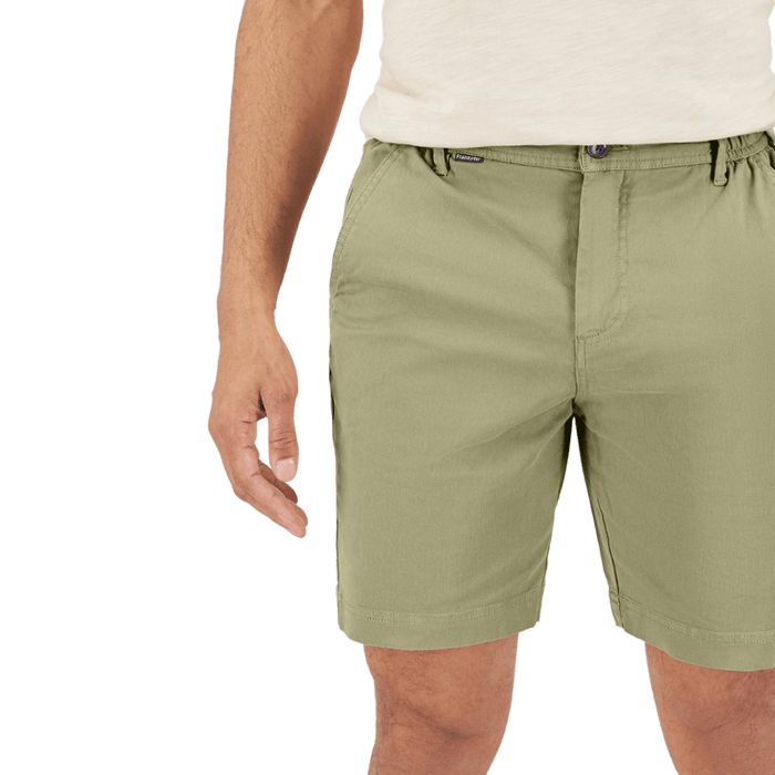Close-up of man wearing light olive green shorts and a cream shirt with hand relaxed at side against plain background