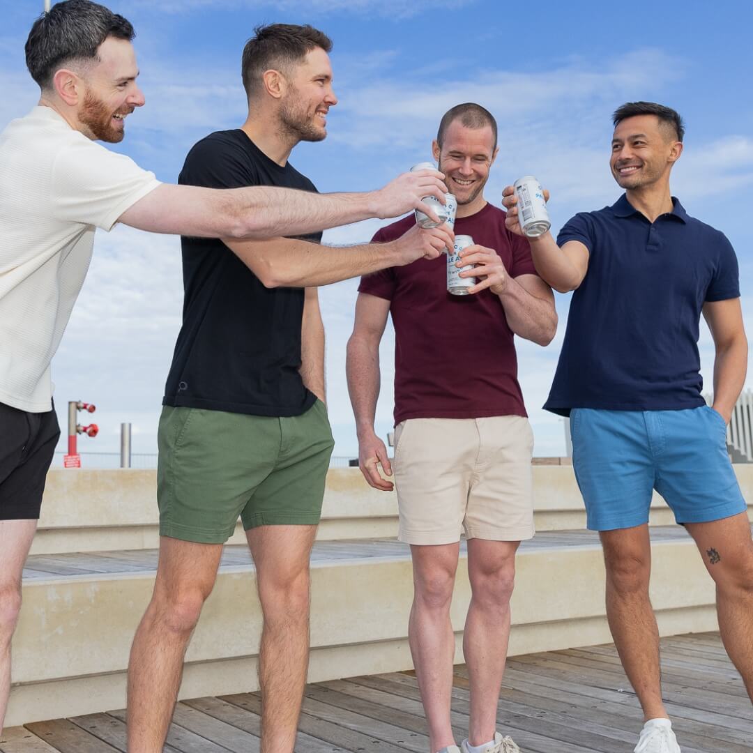 A group of four Australian men wearing The Shorties from Frankster. Each man is drinking a beverage wearing a range of colours including black, green, beige and blue.