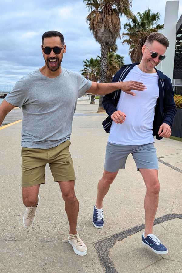 Two men wearing Men's Shorts in khaki and light blue on a sunny palm-lined street by the coast