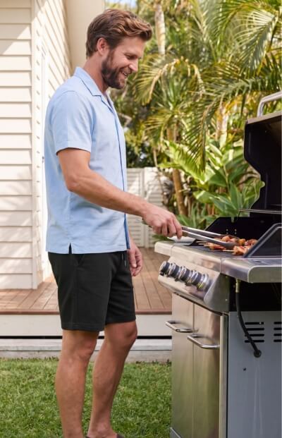 Man wearing black Men's Shorts while grilling outdoors beside a barbecue, showing the casual fabric style and relaxed fit