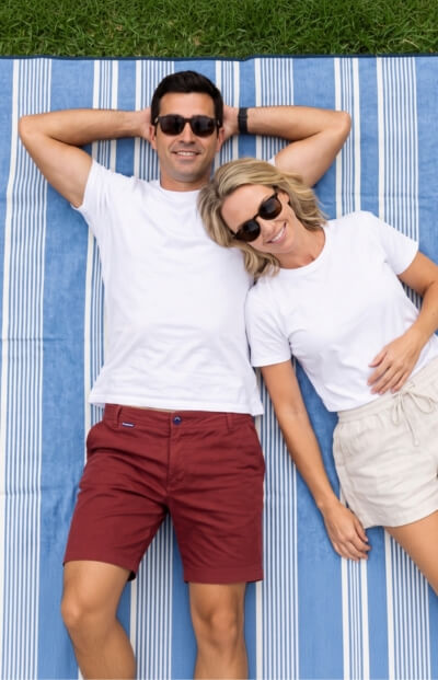 Couple relaxing on a blue striped blanket with the man wearing burgundy Men's Shorts and the woman wearing cream shorts