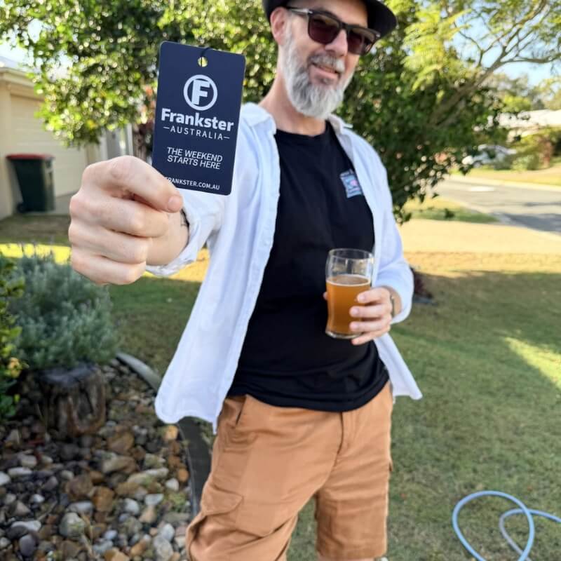 Man wearing tan fabric Men's Shorts outdoors while holding a Frankster Australia tag and a glass of drink