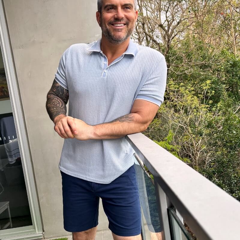 Man wearing navy Men's Shorts made from lightweight fabric while standing on a balcony surrounded by greenery