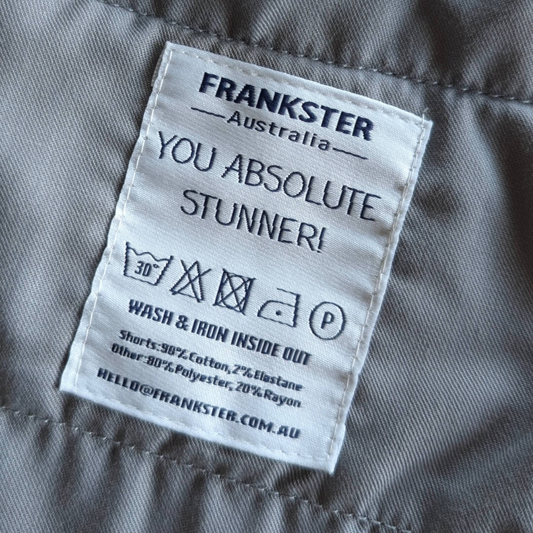 Close-up of a Frankster Men's Shorts care label on grey cotton and elastane fabric with washing instructions