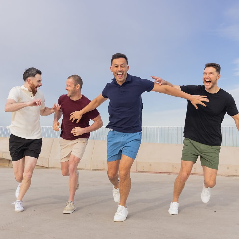 Four men running outdoors in white, black, beige and green Men's Shorts with casual tops and sneakers by the waterfront