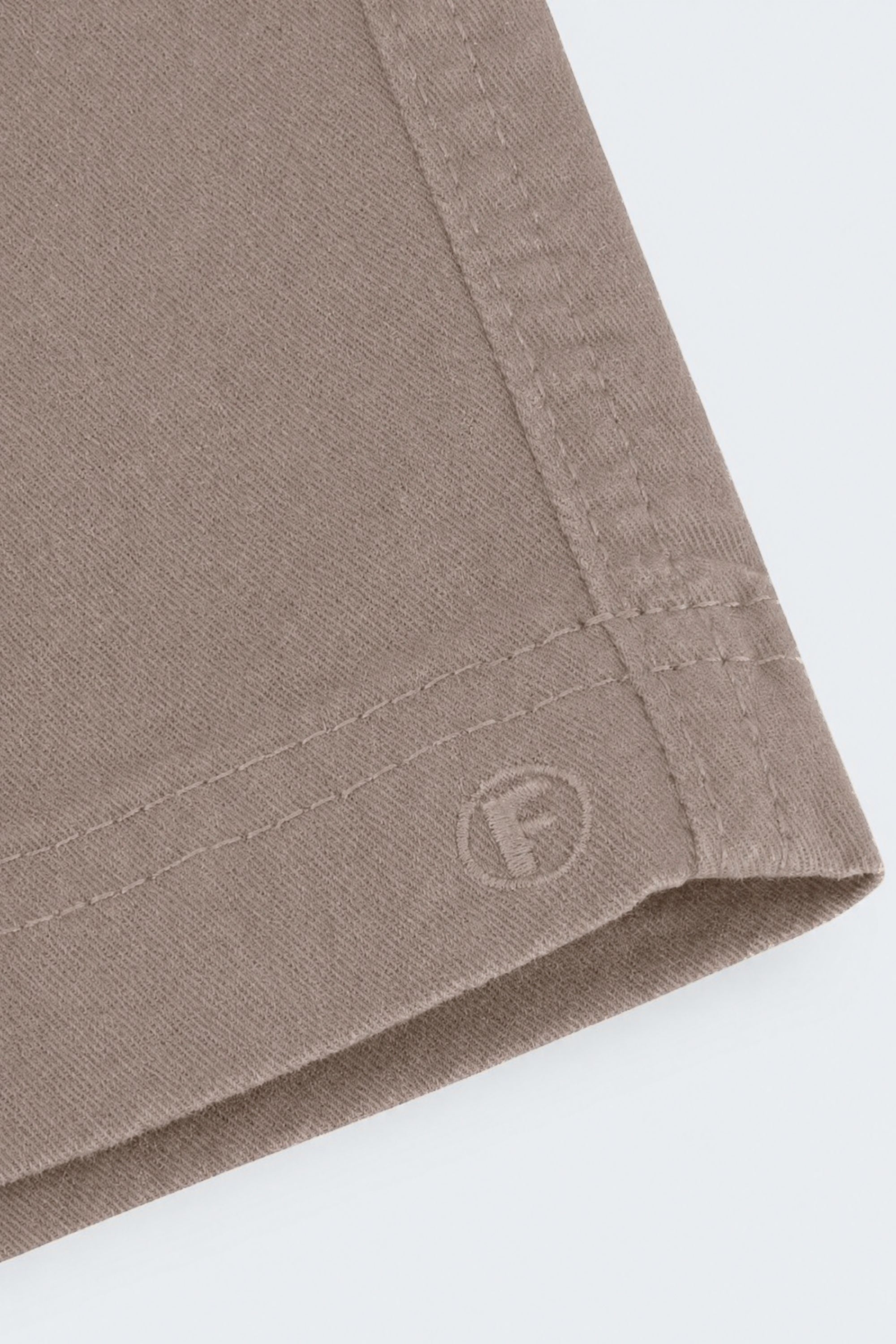 Close-up of taupe-colored men's shorts made from soft, durable fabric with neat stitching and subtle Frankster logo embossing, part of Nomads * The Everydays.