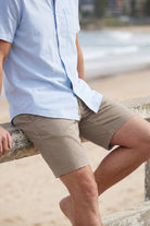 A man sitting by the beach wearing khaki coloured men's shorts made from breathable material, showcasing the comfortable fit of Nomads * The Everydays by Frankster.