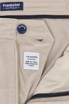 Close-up of beige men's shorts "Shores * The Everydays" by Frankster showing button, zipper, and label sewn inside made from soft, durable cotton material.