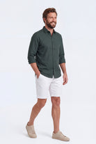 Man wearing Whitecaps * The Everydays men's shorts in white, paired with a dark green shirt, showcasing Frankster’s comfortable, versatile cotton fabric shorts.
