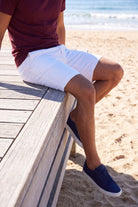 Whitecaps * The Everydays men's shorts in crisp white cotton worn by a man sitting on a wooden bench at the beach, showcasing comfortable casual style by Frankster.