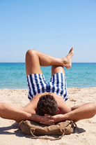 Frankster Cabanas * The Swims Men's Shorts in blue and white striped fabric worn by a man relaxing on a sunny beach