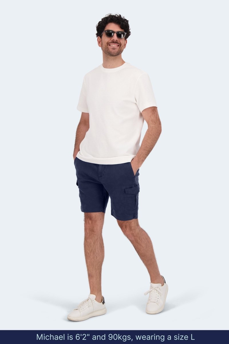 Man wearing Frankster Chillers * The Aussies dark blue cotton cargo men's shorts with white tee and sneakers standing smiling