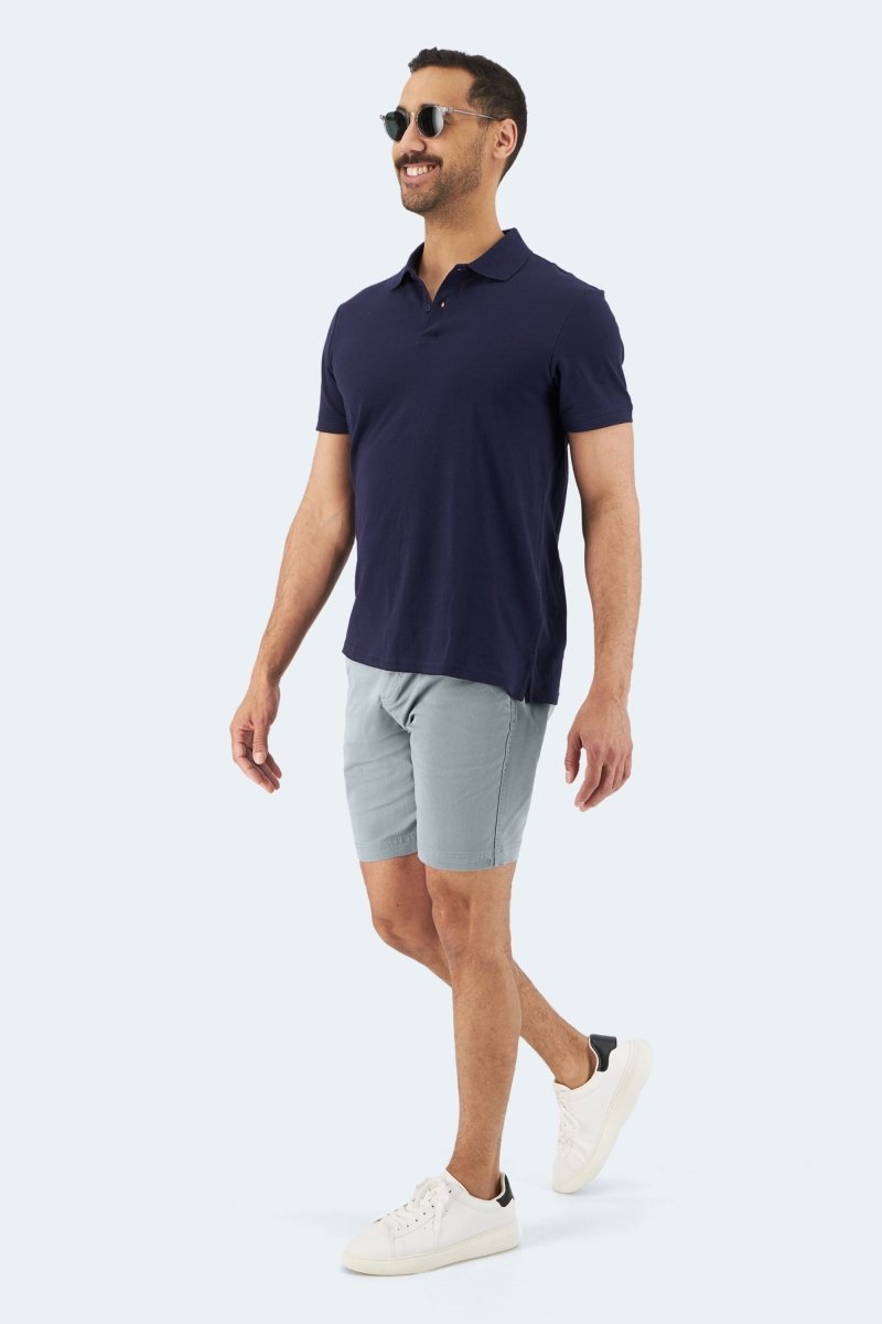 Man wearing Frankster Coastlines * The Everydays men's shorts in blue grey stretch cotton walking with navy polo and white sneakers