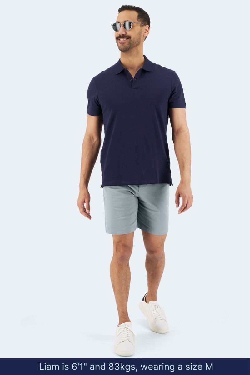 Man wearing Frankster Coastlines * The Everydays light blue grey stretch cotton men's shorts with navy polo and white sneakers walking