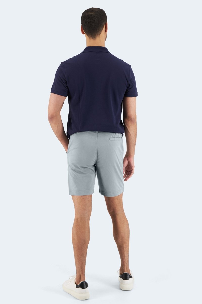 Man wearing Frankster Coastlines * The Everydays light blue grey stretch cotton men's shorts with navy polo and white sneakers standing back view