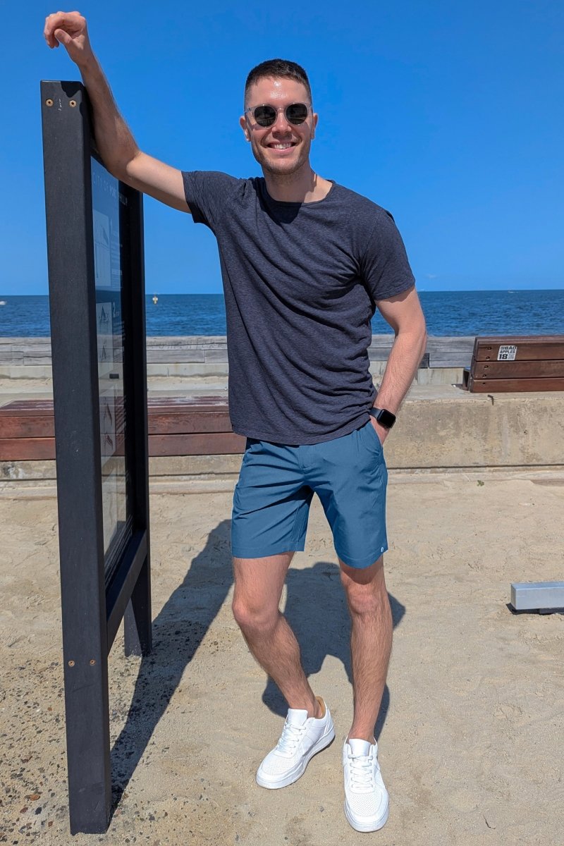 Man wearing mid blue Frankster Harbors * The Actives men's shorts in lightweight breathable fabric outdoors by the beach