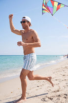 Frankster Lagunas * The Swims men's shorts in light blue and white striped fabric worn on a sunny beach, stylish swim shorts for men