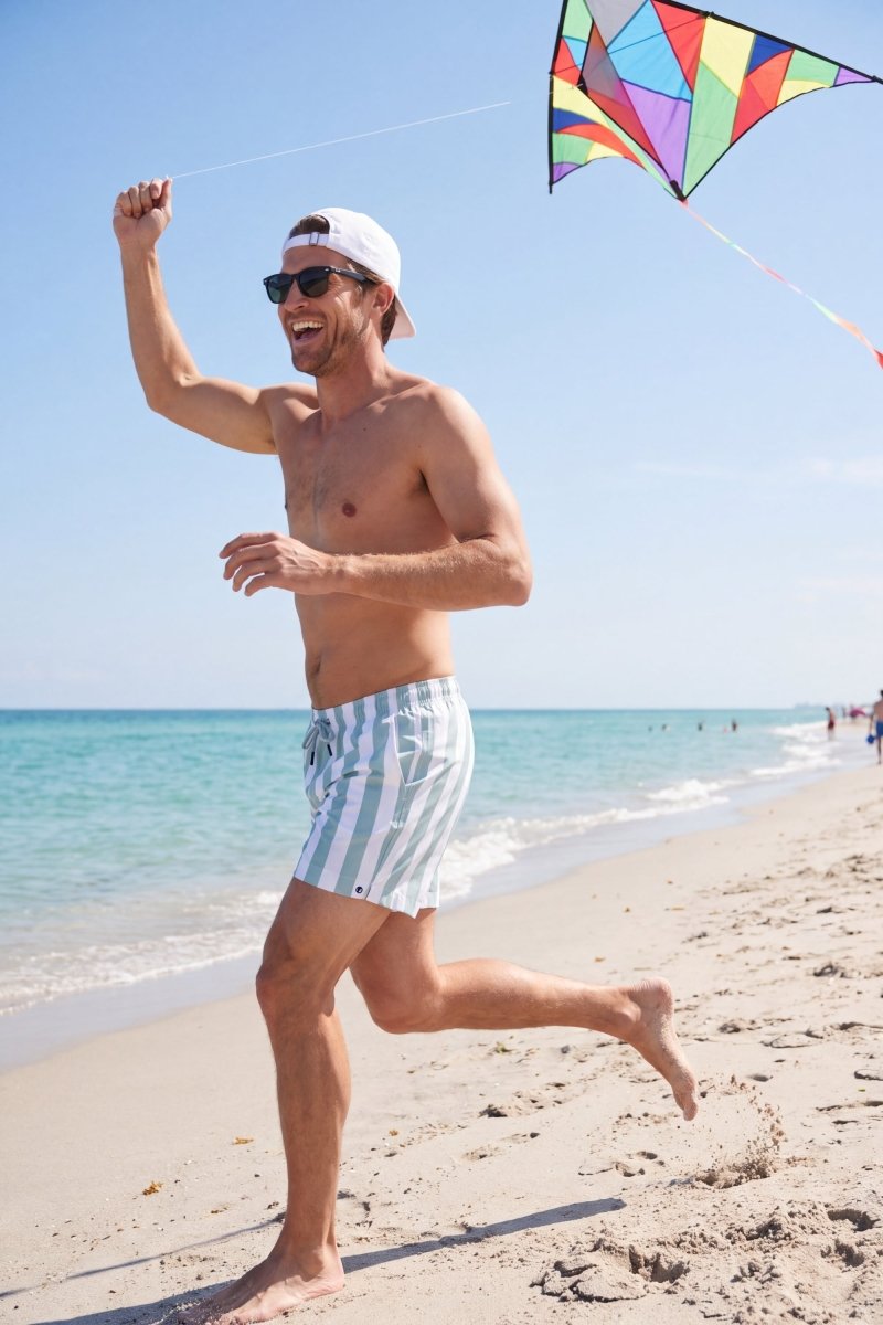 Frankster Lagunas * The Swims men's shorts in light blue and white striped fabric worn on a sunny beach, stylish swim shorts for men