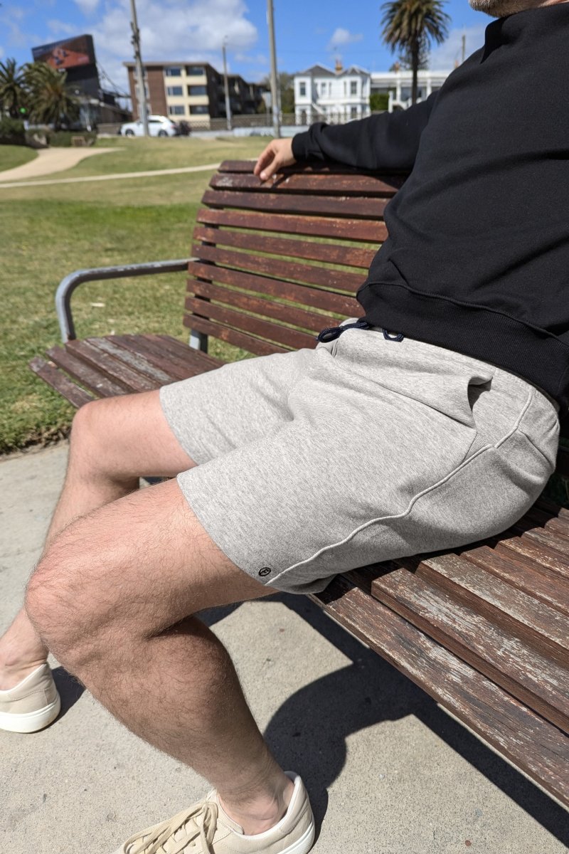 Man sitting on a bench wearing Frankster Lunars * The Comfies light grey cotton men's shorts and white sneakers outdoors