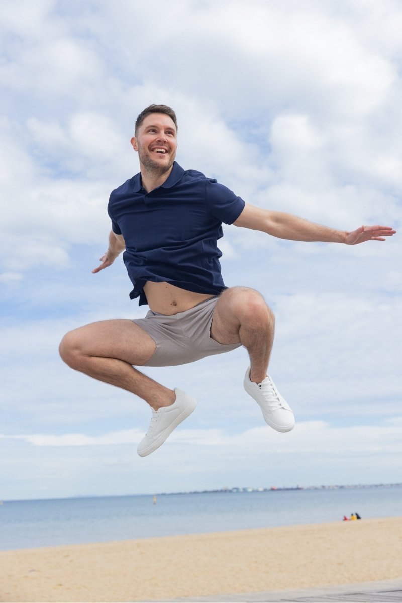 Man jumping on the beach wearing Frankster Lunars * The Shorties light grey stretch cotton men's shorts with white sneakers