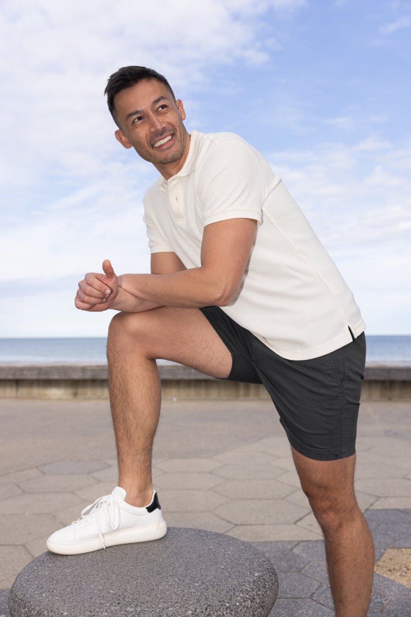 Man wearing Frankster Midnights * The Shorties black stretch cotton men's shorts outdoors by the beach on a sunny day