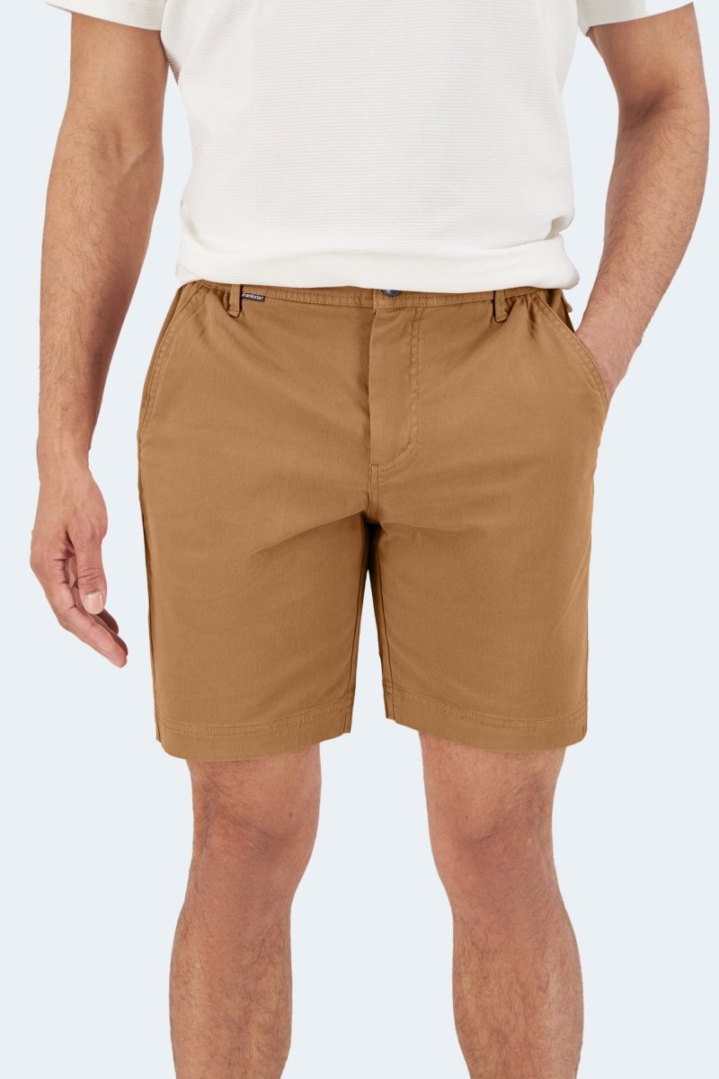 Man wearing Frankster Mokas * The Everydays brown stretch cotton men's shorts with hands in pockets against white background