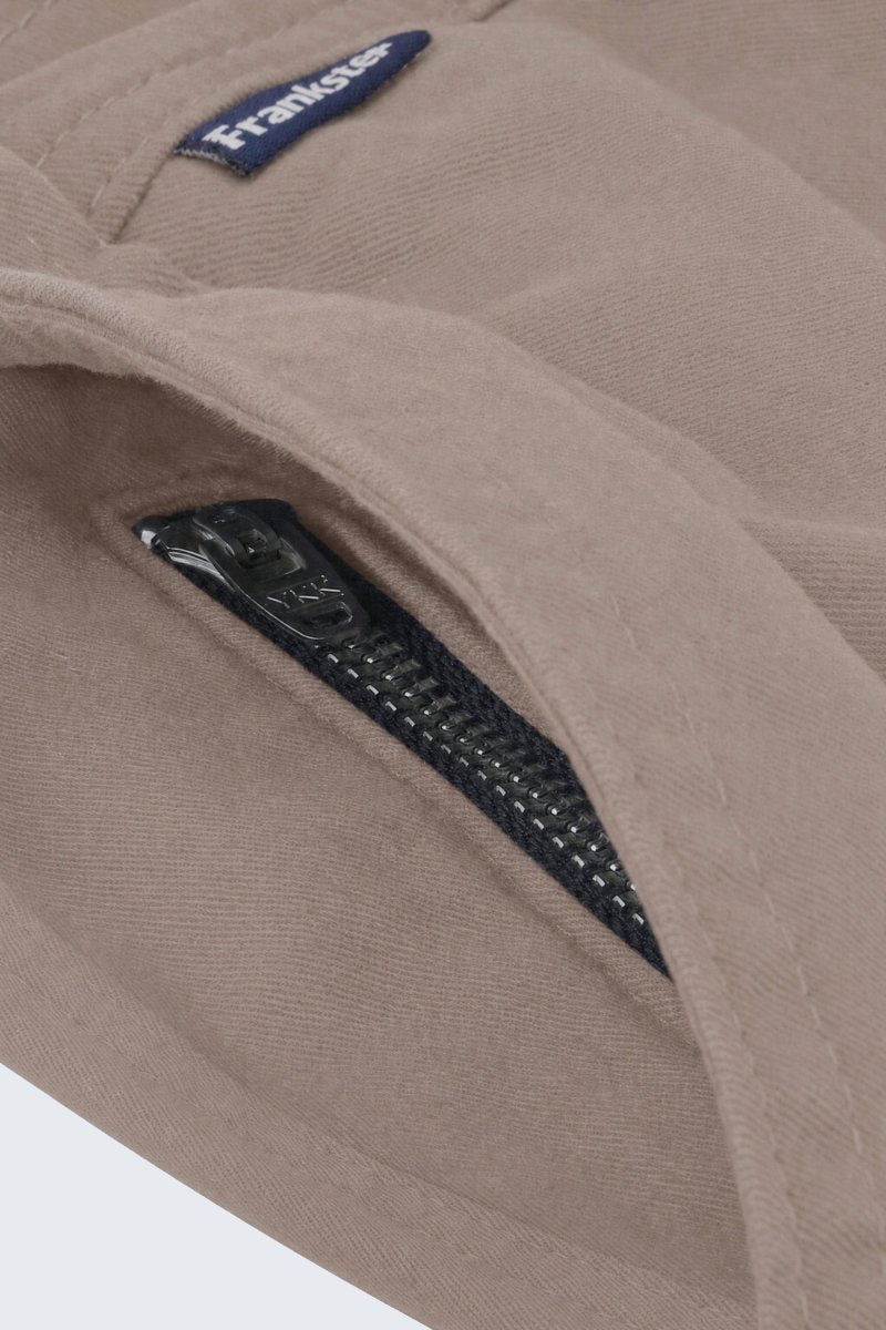 Close-up of beige men's shorts fabric showing a black zipper pocket and a small navy Frankster label, highlighting the durable material of Nomads * The Everydays men's shorts by Frankster.