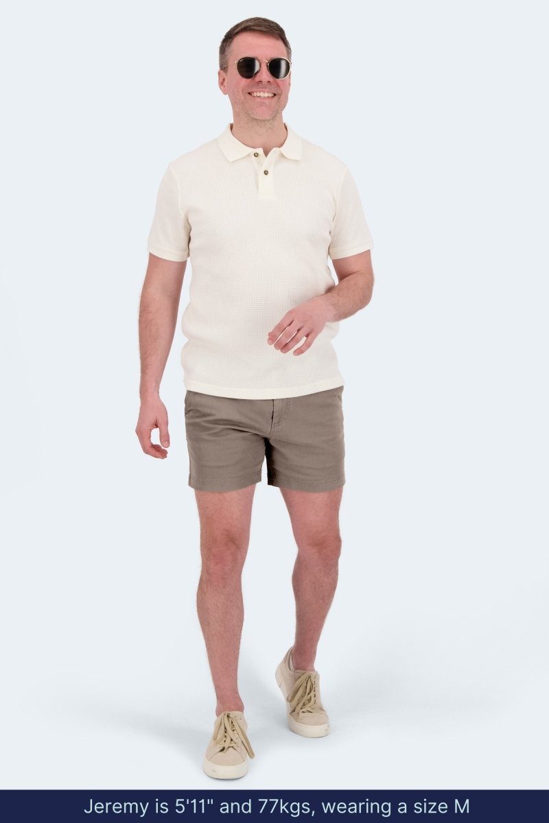 Man wearing Frankster Nomads * The Shorties dark khaki stretch cotton men's shorts with white polo shirt and sneakers walking