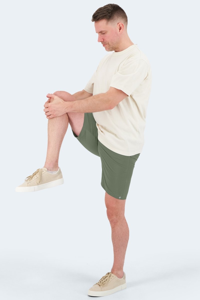 Man wearing army green lightweight cotton Rebels * The Actives men's shorts by Frankster stretching leg outdoors