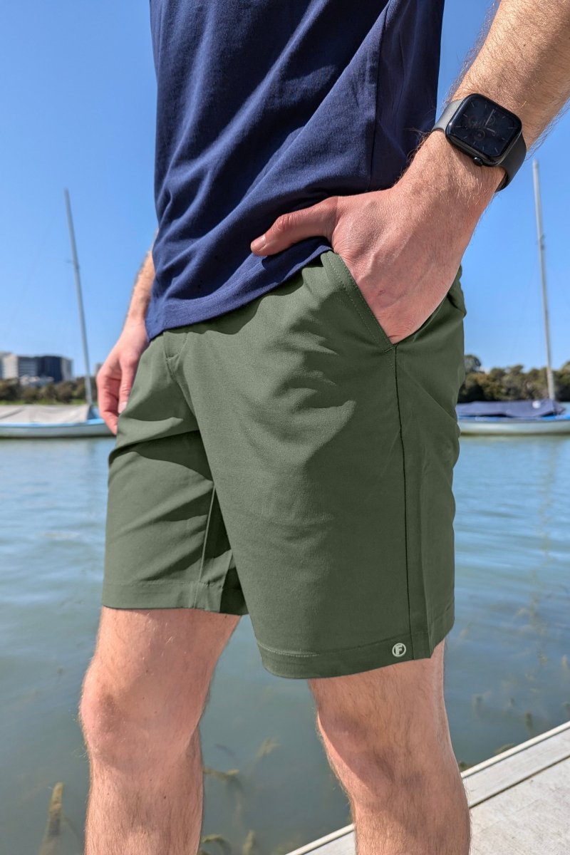 Man wearing Frankster Rebels * The Actives army green lightweight cotton men's shorts by the water on a sunny day