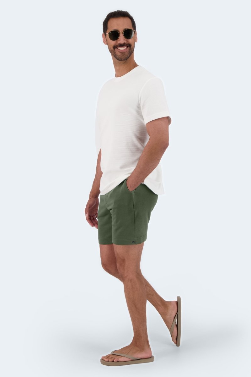 Man wearing Frankster Rebels * The Comfies army green cotton men's shorts with a white t-shirt and sunglasses
