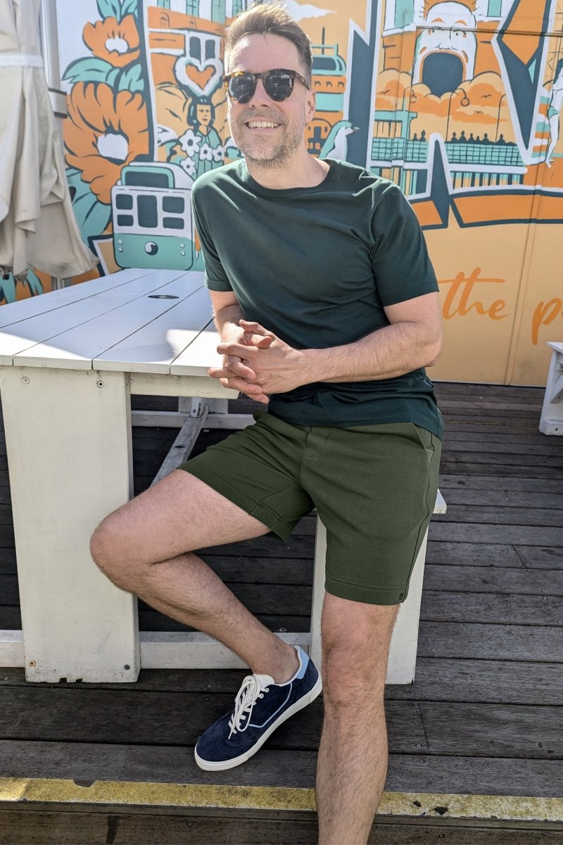 Man wearing Rebels * The Comfies army green cotton men's shorts by Frankster sitting outdoors on a bench