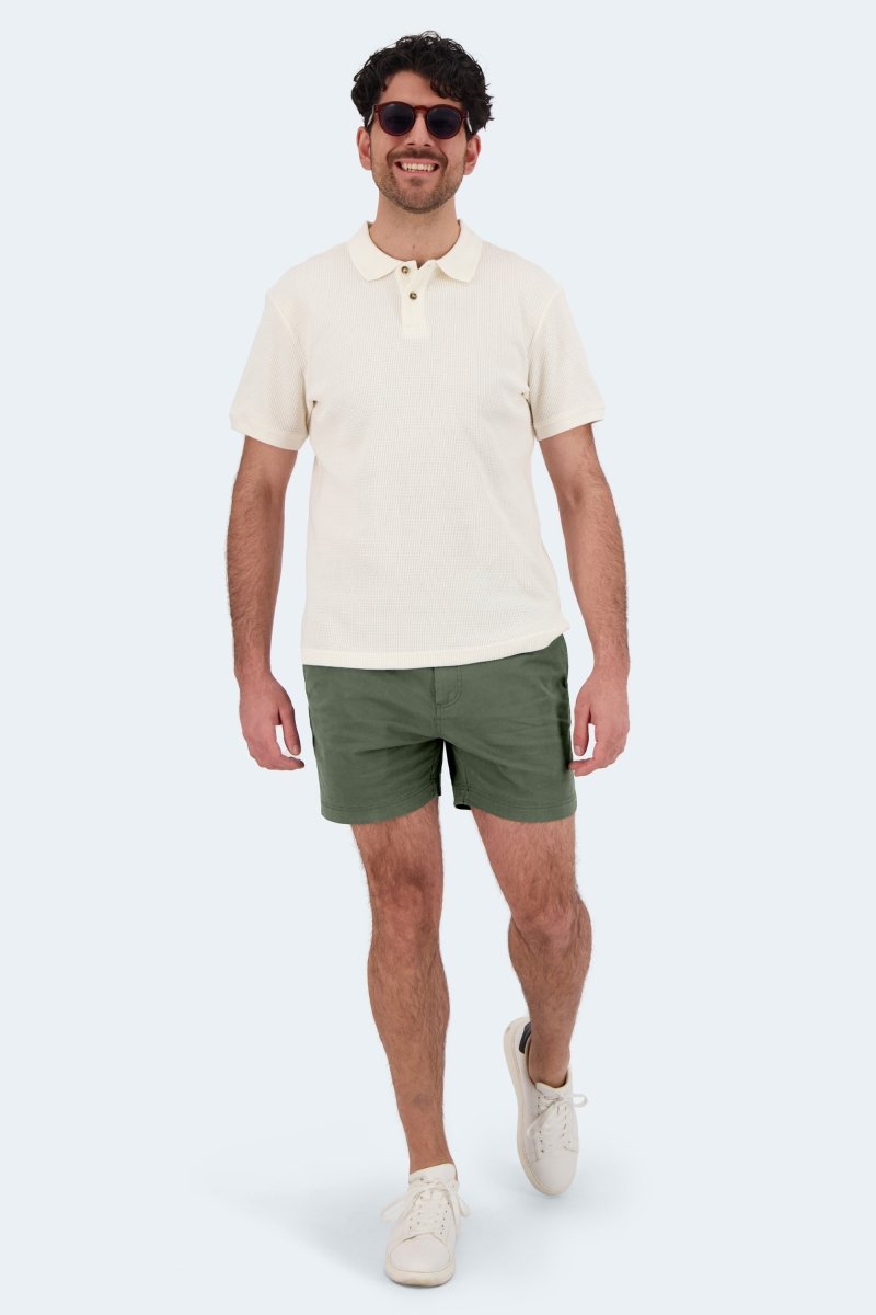 Man wearing Rebels * The Shorties army green stretch cotton men's shorts with beige polo shirt and white sneakers