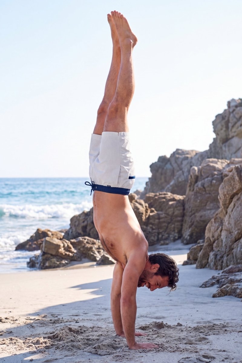 Rivieras * The Swims by Frankster, white fabric Men's Shorts with navy waistband worn on a sunny beach by the sea