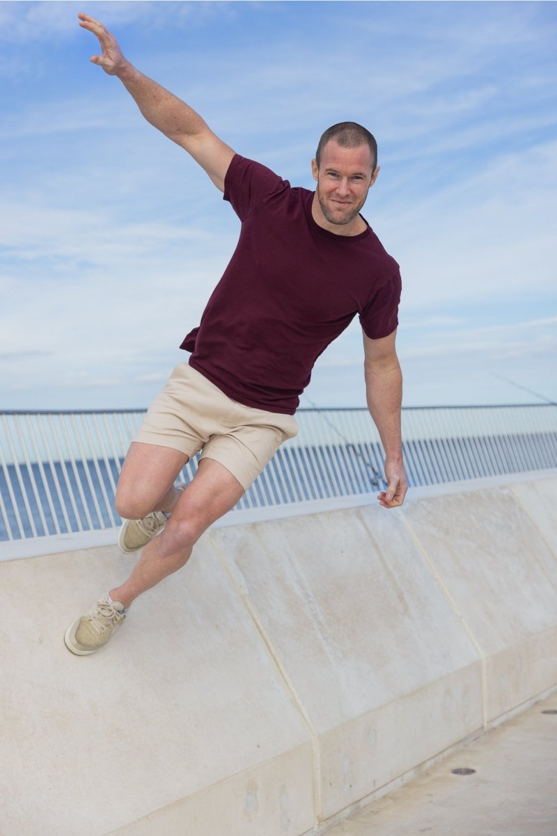 Man wearing Shores * The Shorties light khaki stretch cotton men's shorts and maroon t-shirt outdoors by the ocean