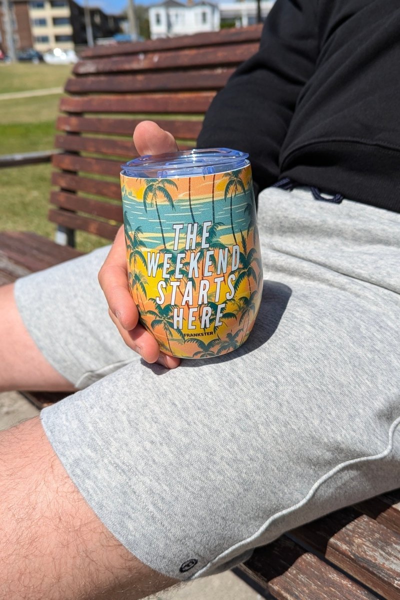Man wearing light gray cotton men's shorts holding The Tropical Weekend Tumbler with palm tree design outdoors