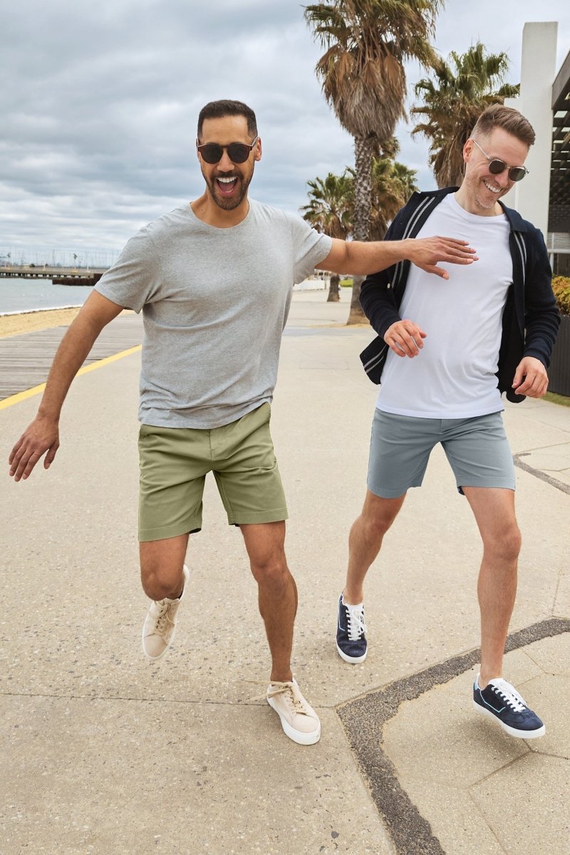 Two men outdoors wearing Frankster Virgins * The Everydays men's shorts in olive green and light blue stretch cotton fabric walking by the beach