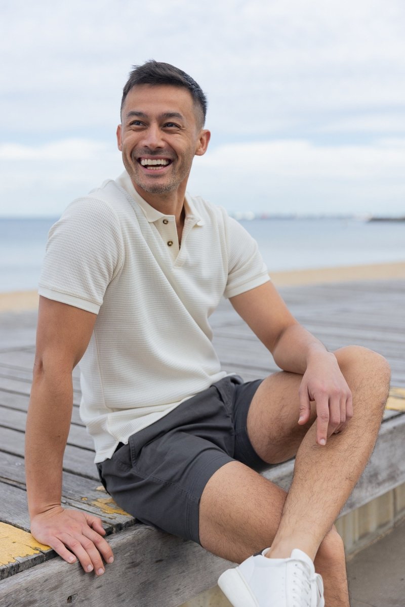 Man wearing Frankster Volcans * The Shorties dark grey stretch cotton men's shorts sitting outdoors by the beach