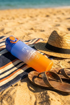 Water Bottle Orange Blue resting on a striped towel beside a straw hat and worn sandals on sandy beach, evoking casual men's shorts day.