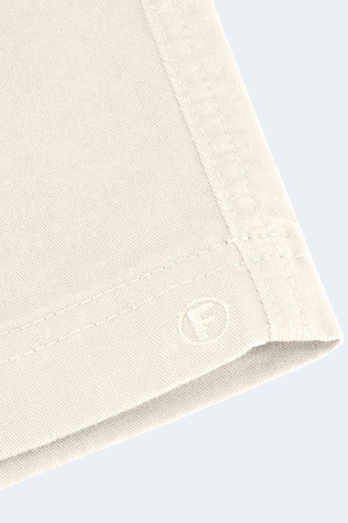 Close-up of the edge of a beige fabric, showcasing stitching details and a small, embossed letter "F" near the corner. The background is a light, solid color, highlighting the texture and craftsmanship of the fabric.